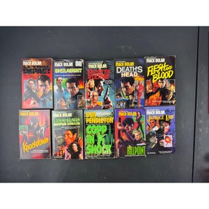 May include: A collection of vintage paperback books featuring action-oriented cover art. The books, titled "Mack Bolan," include titles like "Lethal Impact," "Unslaught," and "Death's Head." The covers showcase illustrations of men with weapons and dramatic scenes.