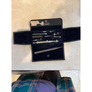 May include: A vintage drafting set in a black case with a blue velvet interior. The set includes various drawing tools, such as compasses, dividers, and a file. The case is open, revealing the tools neatly arranged inside. The text "TWEEN" is visible on a small label.