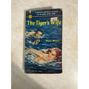 Peut inclure: Un livre de poche vintage intitulé The Tiger's Wife par Wade Miller. La couverture montre une scène d'océan bleu foncé avec un homme et une femme qui nagent. Le texte inclut A novel of a soul-devouring woman, by the author of THE KILLER, 173, 35 cents.