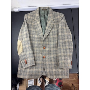 May include: A gray and tan plaid blazer with tan elbow patches and orange buttons. The blazer has a green lining and is a classic style. The blazer is a single-breasted design with a notched lapel.