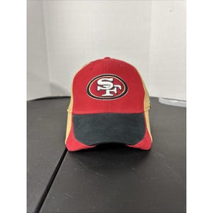 Puede incluir: Gorra de béisbol roja, negra y beige con el logotipo de los 49ers de San Francisco bordado en la parte delantera. El logotipo es un óvalo blanco y rojo con las letras "SF". La gorra tiene una visera curva y una parte trasera de malla.