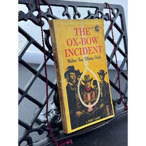 May include: A paperback book titled The Ox-Bow Incident by Walter Van Tilburg Clark with a yellow cover featuring red text and a black and white illustration of men in cowboy hats framed by a white rope noose, published as a Signet Classic.