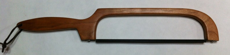 May include: A wooden-handled saw with a black metal blade. The handle is made of light brown wood and has a loop at the end for hanging.