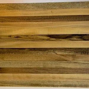 May include: A rectangular wooden cutting board with a striped pattern. The board is made of various shades of brown wood, creating a visually appealing design. The wood grain is visible, adding to the natural aesthetic. This board is suitable for kitchen use.