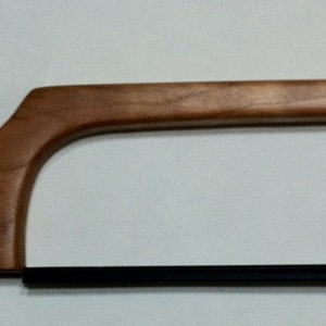 May include: A wooden-handled saw with a black metal blade. The handle is made of light brown wood and has a leather loop at the end.