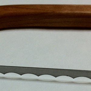 May include: A wooden handled cheese knife with a serrated blade. The blade has a scalloped edge.