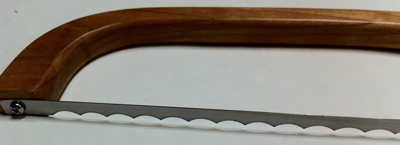 May include: A wooden handled cheese knife with a serrated blade. The blade has a scalloped edge.