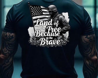 May include: Black t-shirt featuring an American flag and a soldier graphic. The text "Land of the Free Because of the Brave" is displayed below the soldier and flag. The design includes floral accents.