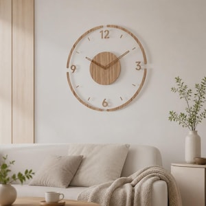 Könnte beinhalten: Eine kreisförmige Wanduhr mit einer hellen Holzmaserung am äußeren Ring, dem zentralen Zifferblatt und den Ziffern 3, 6, 9 und 12. Die Uhr hat dünne, passende Zeiger aus Holz vor einem klaren, offenen Hintergrund.