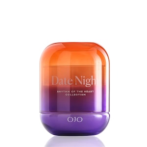 May include: A cylindrical glass container with an ombre effect, transitioning from orange to purple. The text "Date Night" is displayed on the front, with "Rhythm of the Heart Collection" below. The base of the container is purple, with the brand name "OJO" at the bottom.