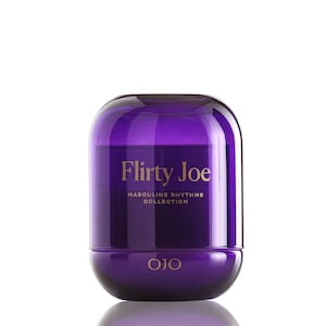 Puede incluir: Una vela de vidrio morado oscuro con forma redondeada. El texto "Flirty Joe" está escrito en letras doradas, con "Masculine Rhythms Collection" debajo. La marca "OJO" está en la base. Fondo blanco.