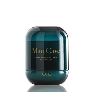 May include: A teal-colored glass jar with a rounded top and base. The words "Man Cave" are printed in gold lettering, along with "Masculine Rhythms Collection." The brand name "OJO" is printed at the bottom.