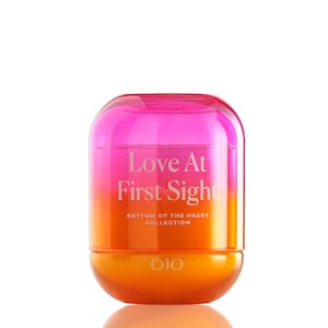 May include: A vibrant, two-toned container with a rounded top and base. The top is a gradient of pink to orange, with the words "Love At First Sight" in white. The bottom is a solid orange. The text "Rhythm of the Heart Collection" is below the main text.