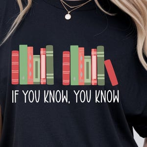 May include: Black t-shirt with a graphic of colorful books arranged in a row. The text "IF YOU KNOW, YOU KNOW" is printed in white below the books. The design features red, green, and pink book spines.