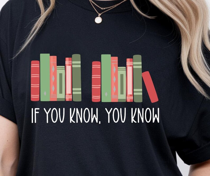 May include: Black t-shirt with a graphic of colorful books arranged in a row. The text "IF YOU KNOW, YOU KNOW" is printed in white below the books. The design features red, green, and pink book spines.