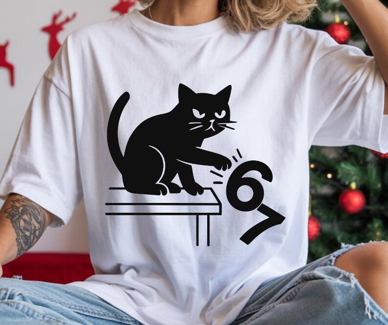 Pu&ograve; includere: T-shirt bianca con grafica di un gatto nero. Il gatto sembra colpire i numeri "67". Il design &egrave; minimalista e d'impatto, perfetto per l'uso quotidiano. Il disegno &egrave; stampato su una t-shirt bianca.
