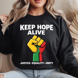 May include: Black sweatshirt with the words "KEEP HOPE ALIVE" in white. Below the text is a raised fist in yellow, green, and red. The words "JUSTICE • EQUALITY • UNITY" are printed below the fist.