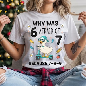 Könnte beinhalten: Weißes T-Shirt mit einer Grafik einer Ente mit Sonnenbrille und Kappe, die Roller fährt. Der Text auf dem Shirt lautet "WHY WAS 6 AFRAID OF 7 BECAUSE 7-8-9". Das Design umfasst Blitze, Blumen, einen Bleistift und eine Erdbeere.