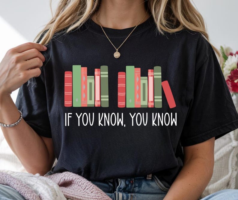 May include: Black t-shirt featuring a graphic of colorful books and the text "IF YOU KNOW, YOU KNOW" in white. The books are in shades of red, green, and pink. The shirt is a comfortable, casual style.