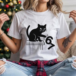 Pu&ograve; includere: T-shirt bianco con un disegno di gatto nero. Il gatto &egrave; seduto su un tavolo e sembra colpire i numeri 6 e 7. La maglietta &egrave; realizzata in un materiale morbido.