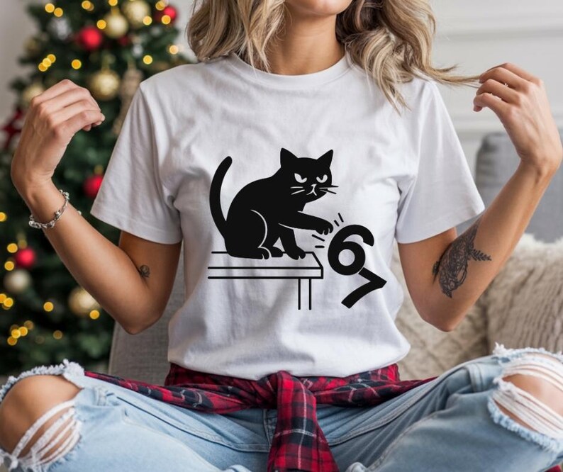 Pu&ograve; includere: T-shirt bianco con un disegno di gatto nero. Il gatto &egrave; seduto su un tavolo e sembra colpire i numeri 6 e 7. La maglietta &egrave; realizzata in un materiale morbido.