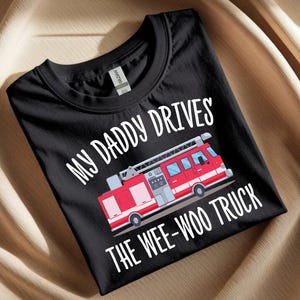 Peut inclure: T-shirt noir avec l'inscription blanche "MY DADDY DRIVES THE WEE-WOO TRUCK". Un camion de pompiers rouge avec une échelle est imprimé en dessous. Le t-shirt est en matière souple.