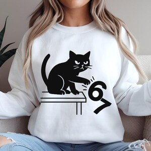 Pu&ograve; includere: Felpa bianca con un disegno di gatto nero. Il gatto &egrave; raffigurato mentre rovescia i numeri 6 e 7. Il gatto ha un'espressione arrabbiata. La felpa &egrave; in stile casual.
