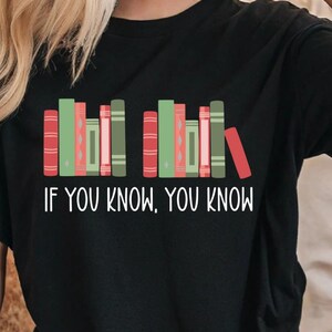 May include: Black t-shirt featuring a graphic of colorful books in red, green, and pink. The text "IF YOU KNOW, YOU KNOW" is printed in white below the books. A casual, comfortable tee for book lovers.