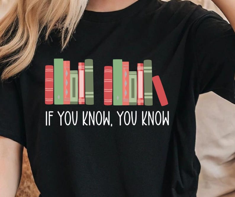 May include: Black t-shirt featuring a graphic of colorful books in red, green, and pink. The text "IF YOU KNOW, YOU KNOW" is printed in white below the books. A casual, comfortable tee for book lovers.