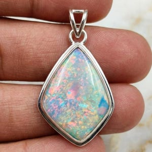 May include: A silver pendant featuring a pear-shaped opal gemstone. The opal exhibits a vibrant play of colour, including shades of blue, pink, and green. The pendant has a simple, elegant design, suitable for everyday wear or special occasions.