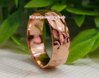 May include: A copper-colored ring with a hammered texture. The ring is set against a backdrop of green leaves and a white surface. The text "Kiranjewellryhub" is visible on the ring.