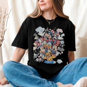 May include: Black t-shirt featuring a colorful graphic of Disney characters, including Mickey Mouse, Minnie Mouse, Donald Duck, and Pluto, in patriotic attire. The design incorporates American flags and the text "America 250th USA Anniversary".