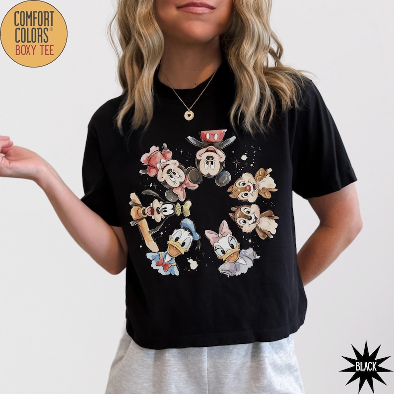 May include: Black Comfort Colors boxy tee featuring a circular graphic of cartoon characters including Mickey Mouse, Minnie Mouse, Donald Duck, Daisy Duck, Goofy, and Chip and Dale. The shirt has short sleeves and a crew neck.