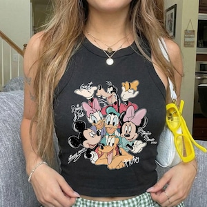 K&ouml;nnte beinhalten: Schwarzes Tanktop mit einer Cartoon-Grafik von Micky Maus, Minnie Maus, Donald Duck, Daisy Duck, Goofy und Pluto. Das Top hat einen runden Ausschnitt und ist &auml;rmellos. Der Text "Mickey Mouse" und "Minnie Mouse" ist unten aufgedruckt.