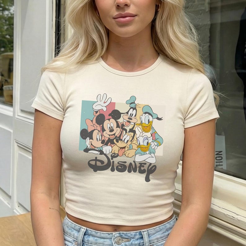 Pu&ograve; includere: T-shirt color crema a maniche corte con grafica Disney. La grafica include Topolino e Minnie, Pippo e Paperino. La parola "Disney" &egrave; stampata in un carattere stilizzato sotto i personaggi.