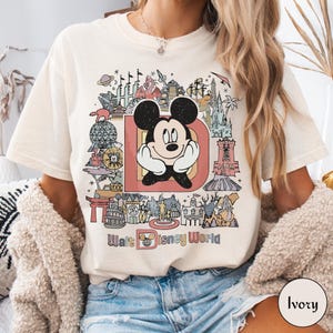 Puede incluir: Camiseta de color marfil con un gr&aacute;fico colorido de Mickey Mouse dentro de una gran letra "D" y varios monumentos de Disney World. Las palabras "Walt Disney World" est&aacute;n impresas debajo. La camiseta tiene un corte relajado.