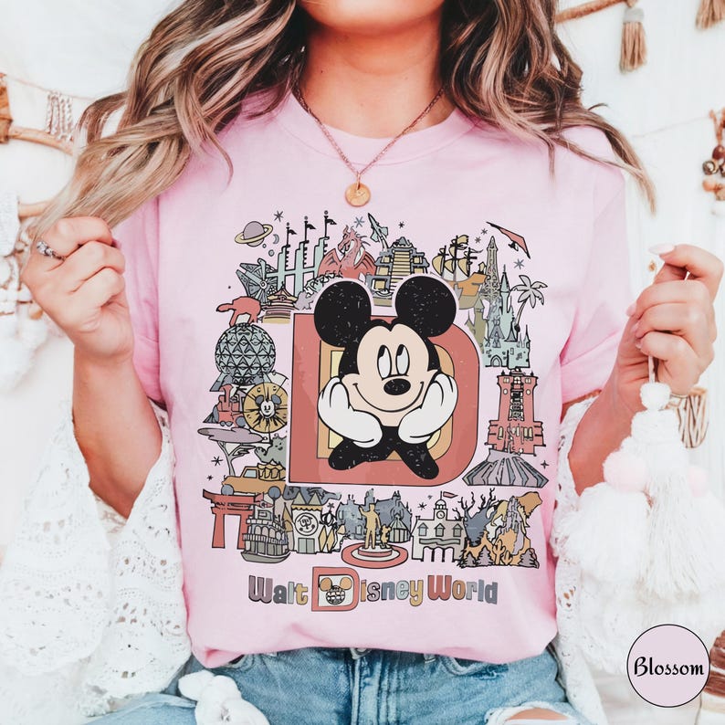 Puede incluir: Camiseta rosa claro con un dibujo de Mickey Mouse dentro de una gran "D" y monumentos de Disney World. Las palabras "Walt Disney World" est&aacute;n impresas debajo en una fuente colorida.