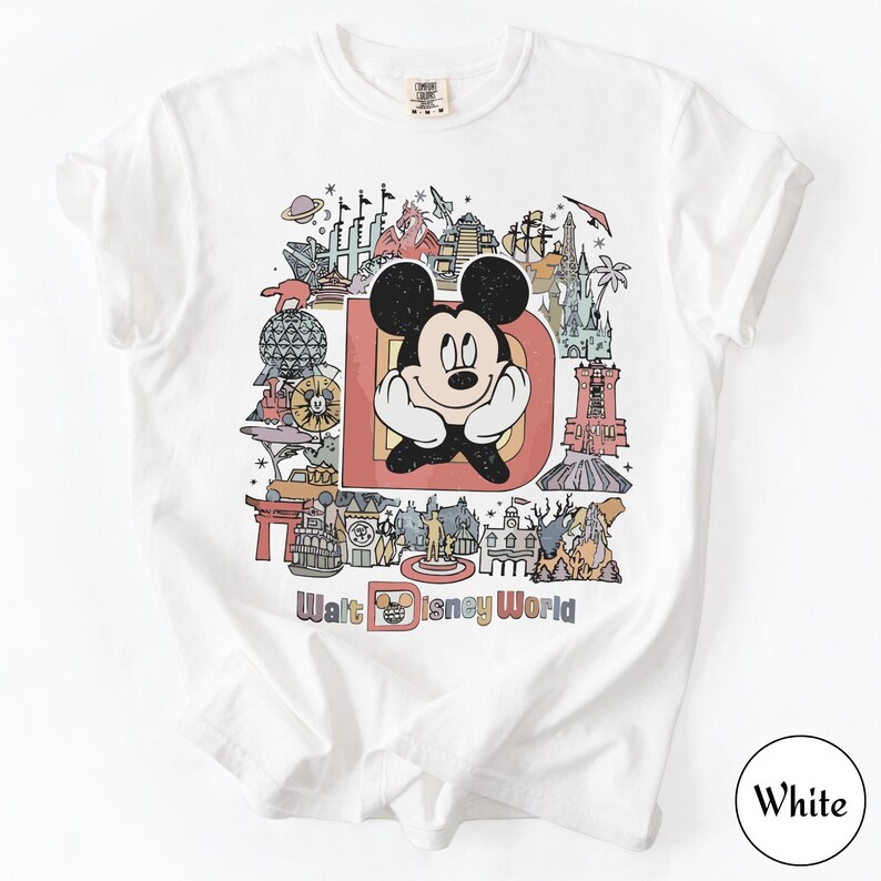Puede incluir: Camiseta blanca con un gr&aacute;fico colorido de Mickey Mouse dentro de una gran "D", rodeado de monumentos de Disney World. Las palabras "Walt Disney World" est&aacute;n impresas en la parte inferior del dise&ntilde;o.
