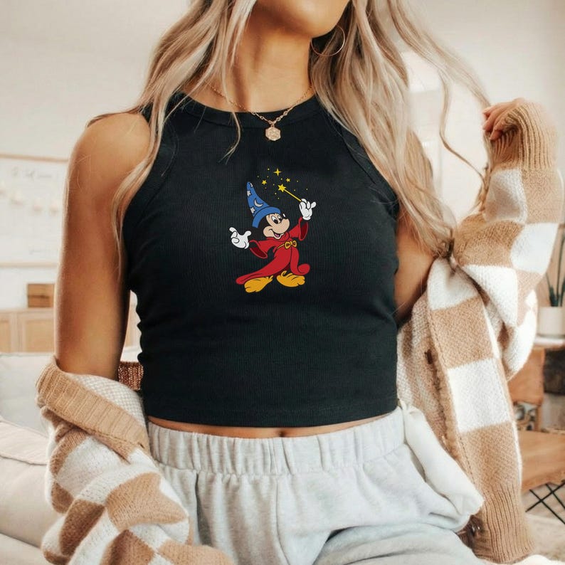 May include: Black ribbed tank top featuring an embroidered image of Mickey Mouse dressed as a wizard, holding a wand with stars. The cartoon character is wearing a blue wizard hat and a red robe. The tank top is sleeveless.