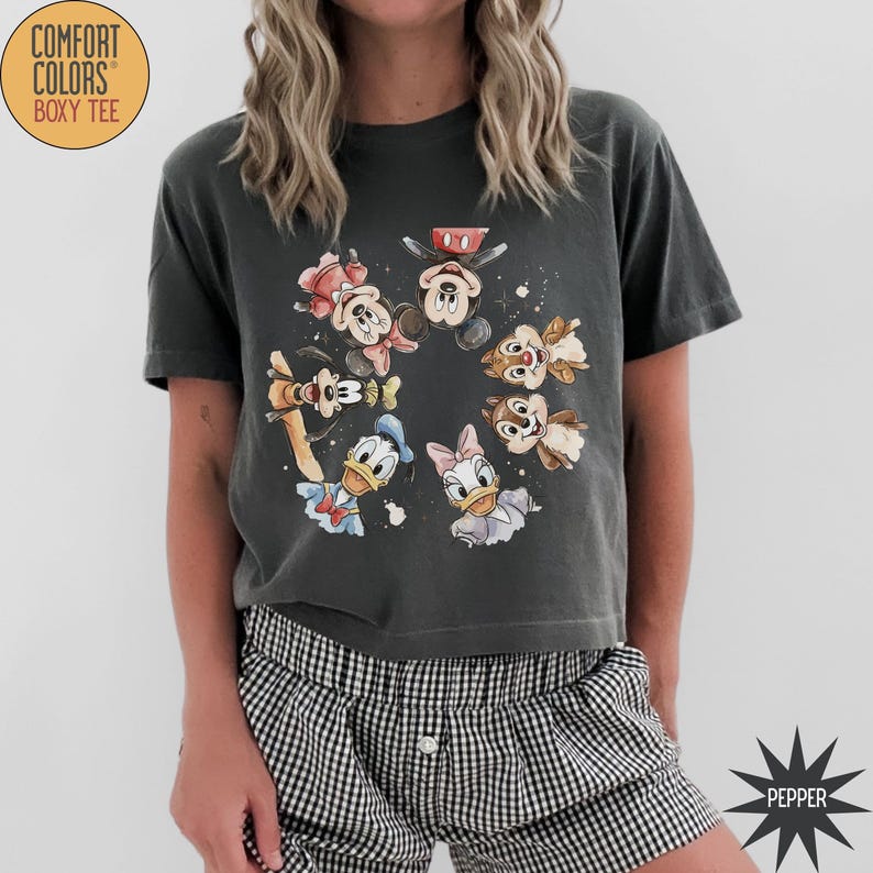 May include: Dark gray Comfort Colors Boxy Tee featuring a watercolor design of Disney characters including Mickey Mouse, Minnie Mouse, Donald Duck, Daisy Duck, Chip, and Dale. The shirt has short sleeves and a crew neck.