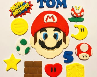 Może przedstawiać: Zbiór kolorowych, jadalnych dekoracji przedstawiających postacie i symbole z serii gier wideo Super Mario. Zawiera twarz Mario, czerwonego grzyba, żółtą gwiazdę i imię "TOM" w kolorze niebieskim.