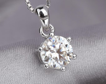 May include: A silver pendant necklace featuring a large, round, clear gemstone. The gemstone is set in a silver prong setting and hangs from a delicate silver chain. The background is a soft, gray fabric.