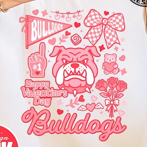 May include: White t-shirt with a pink graphic design featuring a bulldog, hearts, and the text "Happy Valentine's Day Bulldogs." The design includes a bow, roses, and a foam finger. The bottom of the shirt has the text "PNG DIGITAL DOWNLOAD."