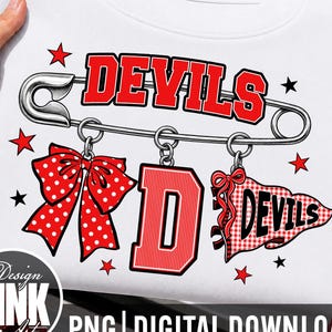 May include: A white sweatshirt featuring a graphic of a large silver safety pin with the word DEVILS in red letters above it. Hanging from the pin are a red polka dot bow, a large red letter D, and a red and white chequered pennant with DEVILS.