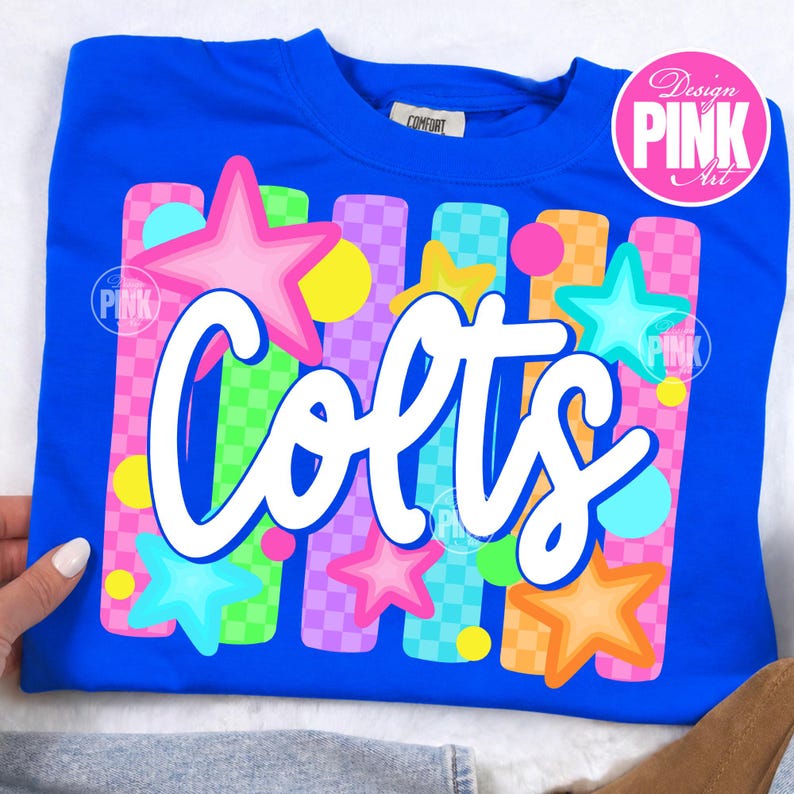 Pu&ograve; includere: Una felpa blu reale con la scritta "Colts" in corsivo bianco. Il design include stelle colorate e strisce verticali in rosa, verde, arancione e viola. La maglia ha uno scollo tondo.