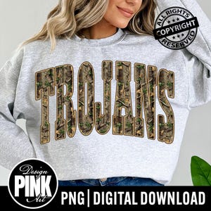 May include: A light gray sweatshirt with the word "TROJANS" in large, block letters filled with a camouflage pattern. The sweatshirt has a crew neck and long sleeves. The image also includes the text "ALL RIGHTS RESERVED" and "Design PINK Art".