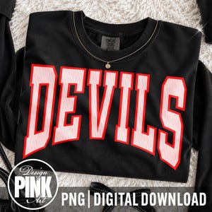 Puede incluir: Una sudadera negra de manga larga con la palabra DEVILS en letras grandes, negritas y con borde rojo, con un patrón de rayas verticales blancas. La etiqueta interior dice COMFORT COLORS. Un collar dorado con un pequeño dije descansa sobre el cuello.