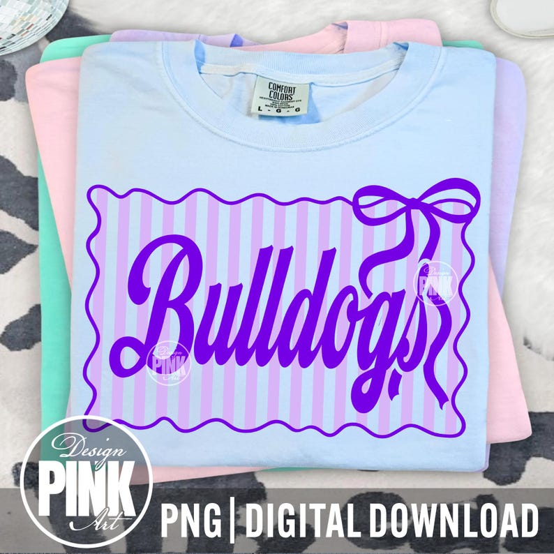 May include: A stack of light blue, pink, and mint green t-shirts. The top shirt is light blue with a purple design that says "Bulldogs" in a script font. The design is framed by a purple scalloped border and a bow. The text "PNG | DIGITAL DOWNLOAD" is at the bottom.