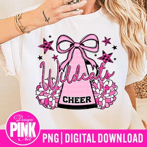 May include: White t-shirt featuring a pink and black design with the word "Wildcats" in a script font. The design includes a pink bow, stars, pom-poms, and the word "CHEER". The bottom of the image has the text "PNG DIGITAL DOWNLOAD".