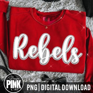 May include: A bright red long-sleeve sweatshirt featuring the word Rebels in a large, white, cursive font with a silver glitter outline. The garment has a crew neckline and a visible interior tag. The design is centered on the front of the shirt.